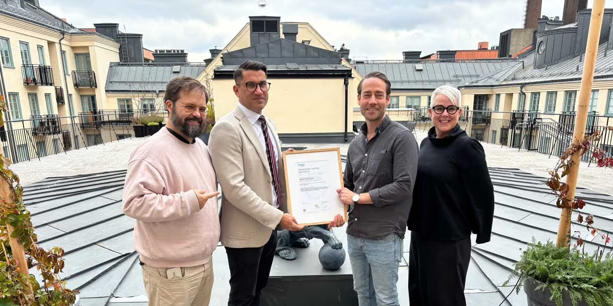 Fyra personer på en takterrass håller upp det inramade ISO/IEC 42001-certifikatet.